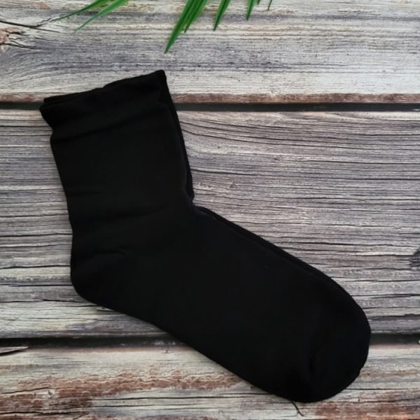 one pair of black socks on wood table with green leaves